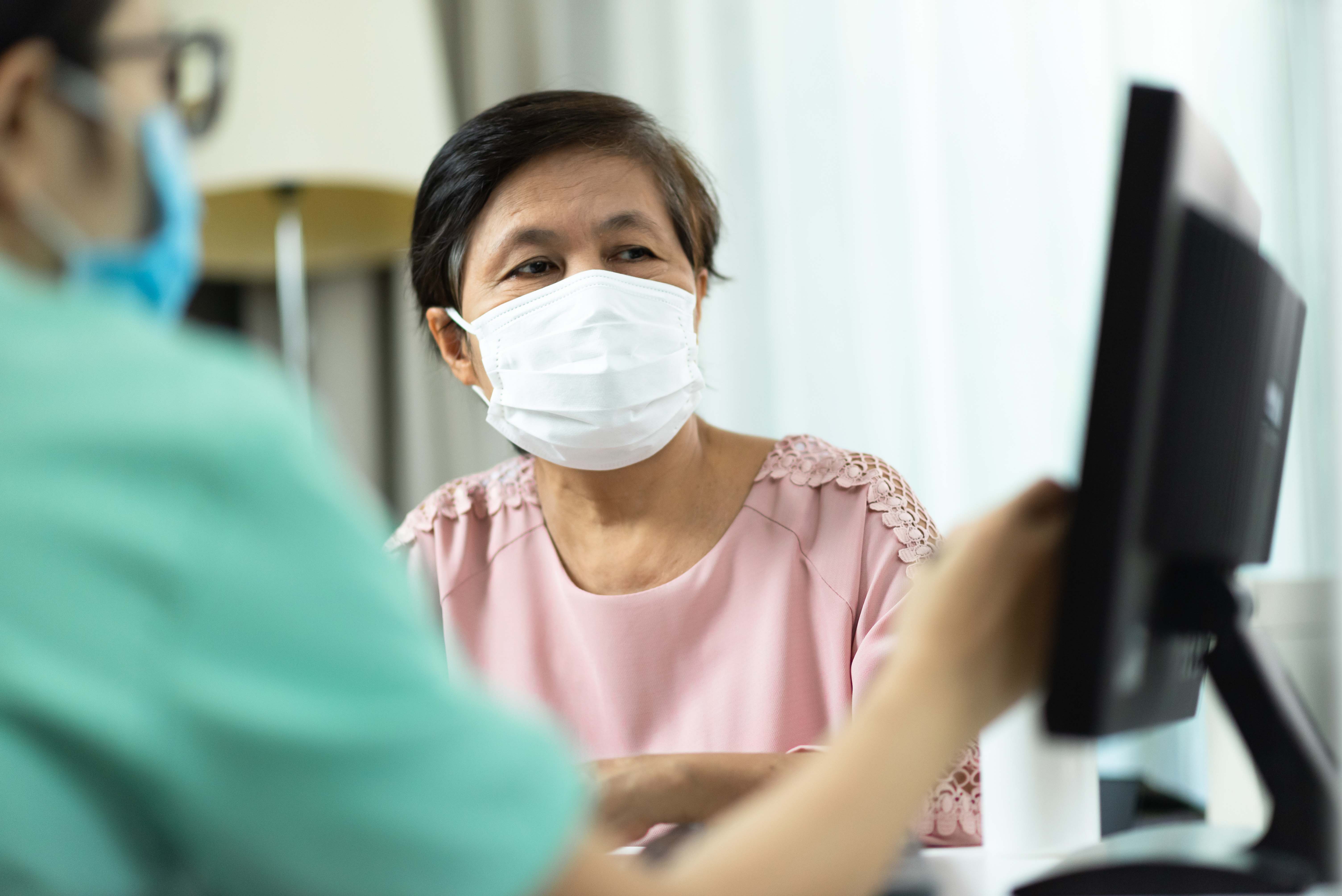 Asian American woman speaks with health care provider with masks on