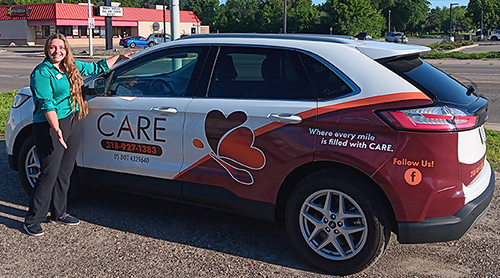 Care staff member stands next to company car