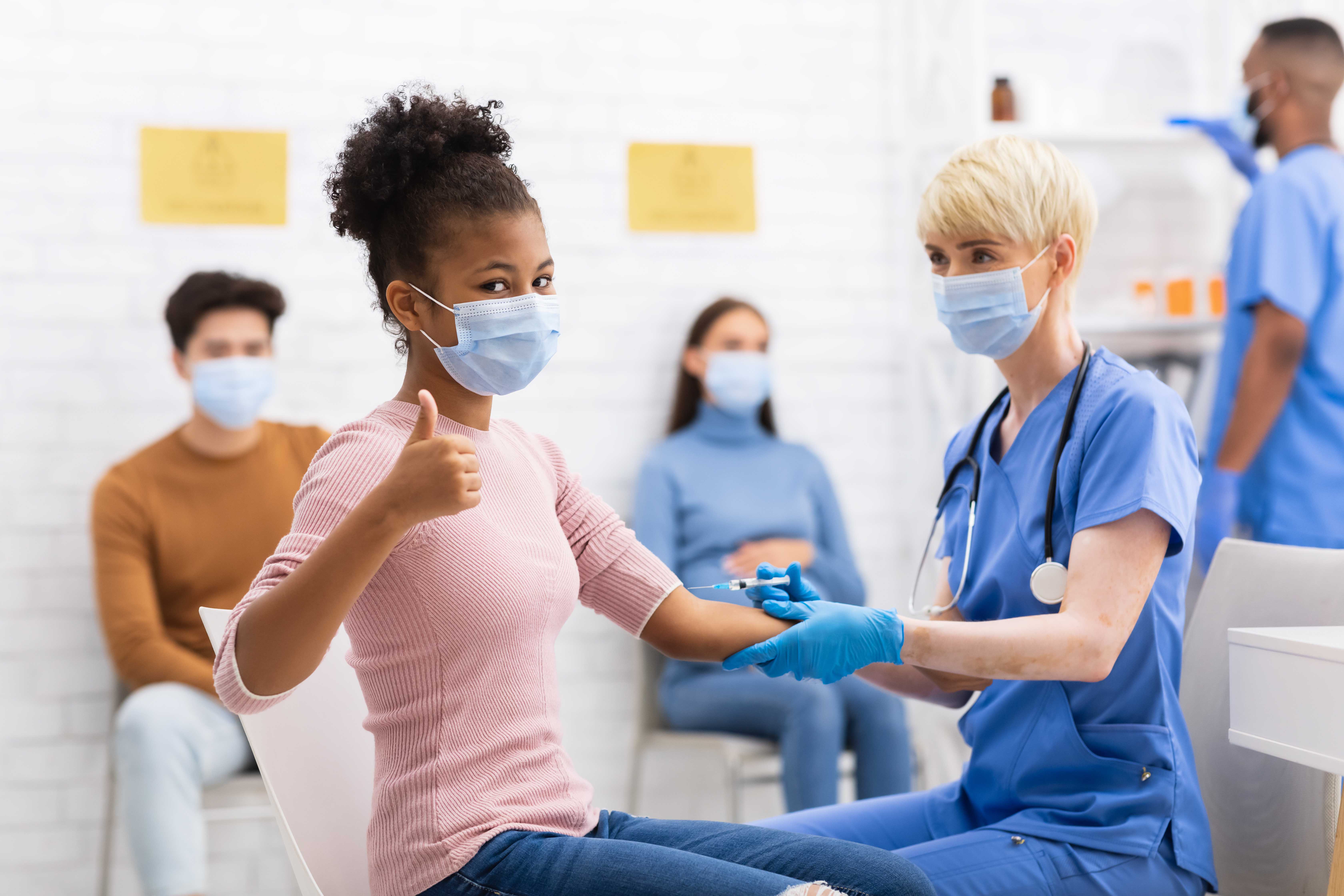 kid showing thumbs up while getting a vaccine