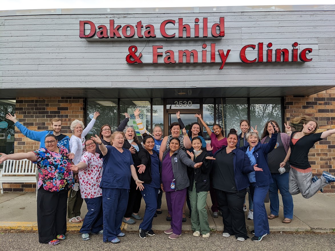 DCFC staff are smiling with their arms extended, in front of the clinic building