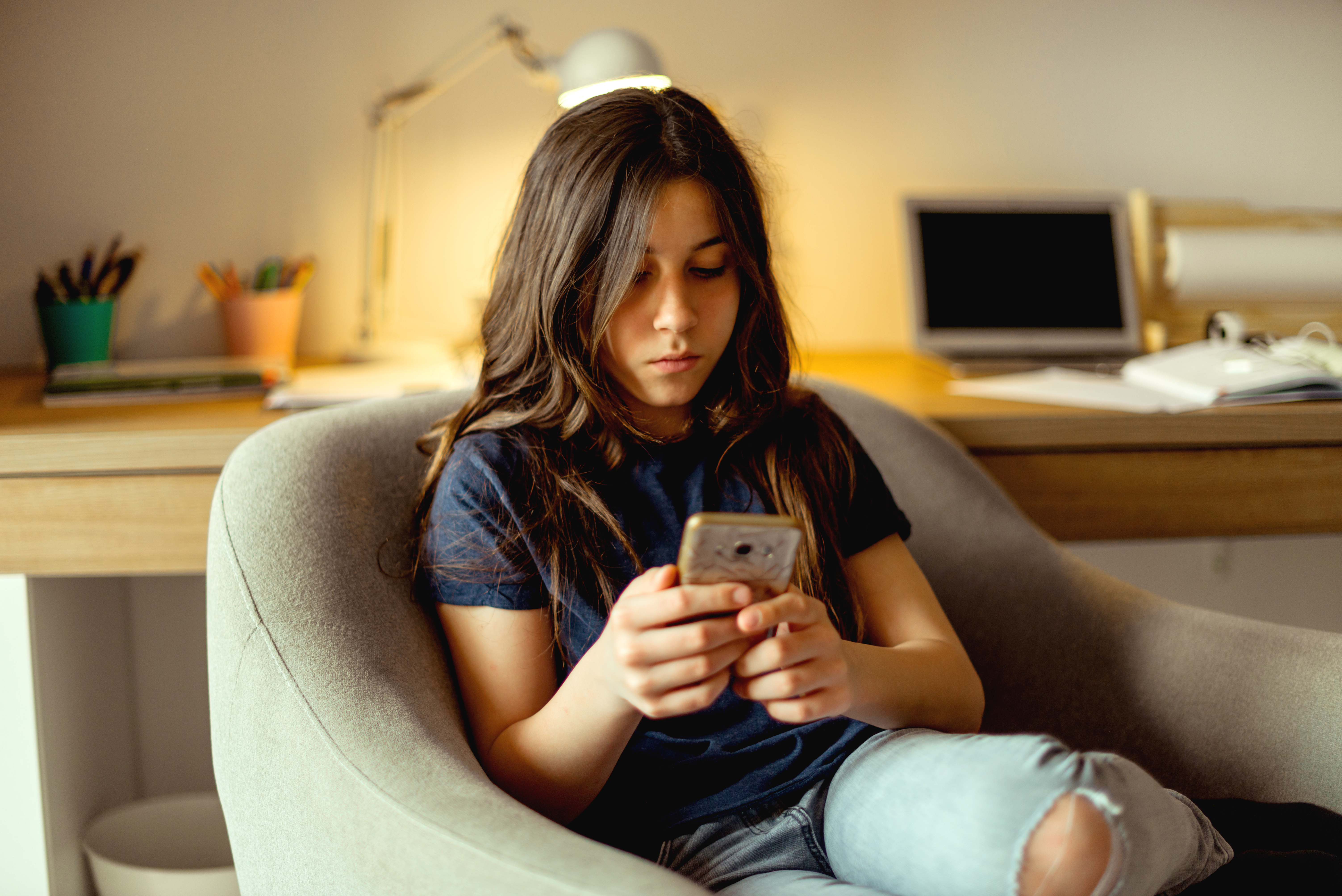 Female-presenting teen sitting in chair and looking at cell phone