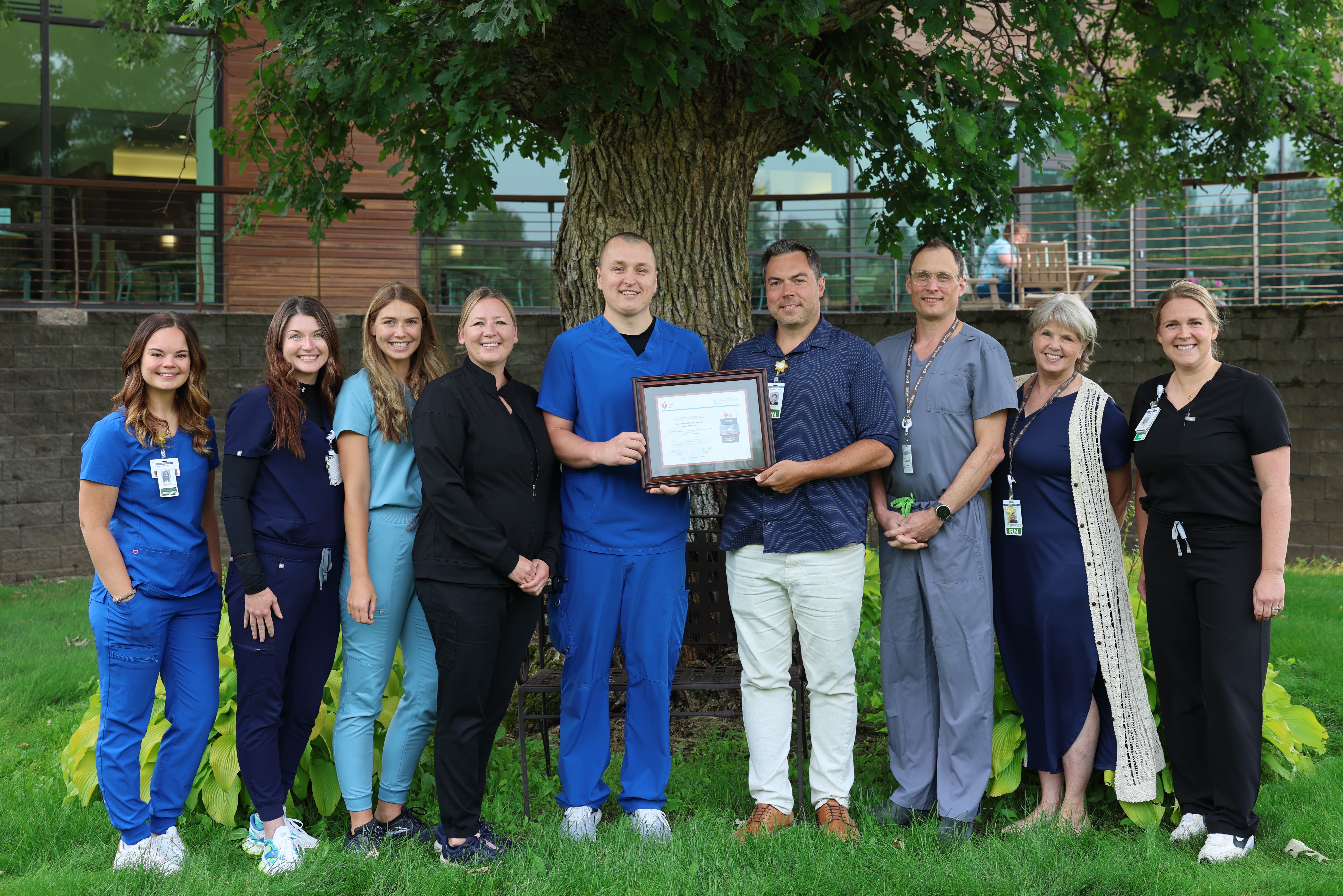 Grand Itasca staff stand in front of a tree holding an award.