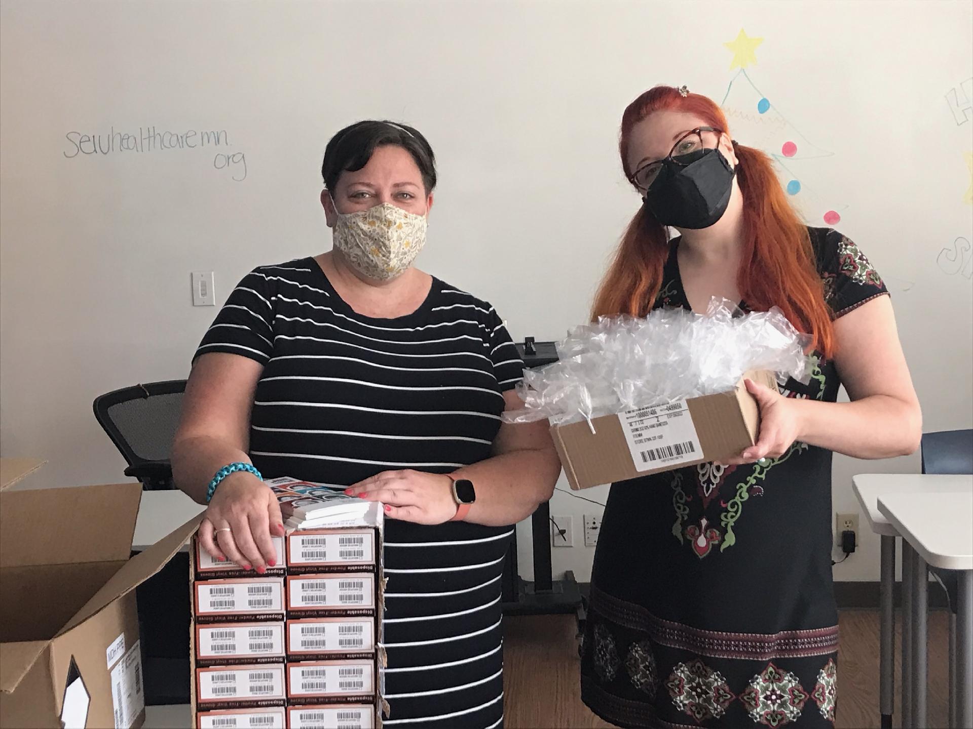 two healthcare workers holding boxes of COVID-19 tests for the disability community