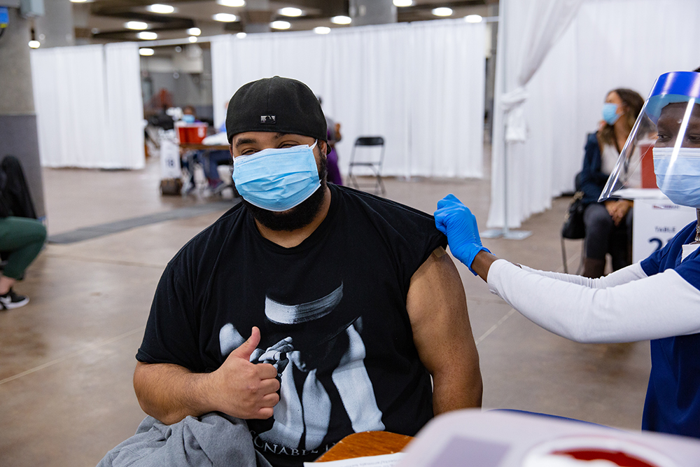 Man wearing mask giving a thumbs up while health care worker puts bandage on arm