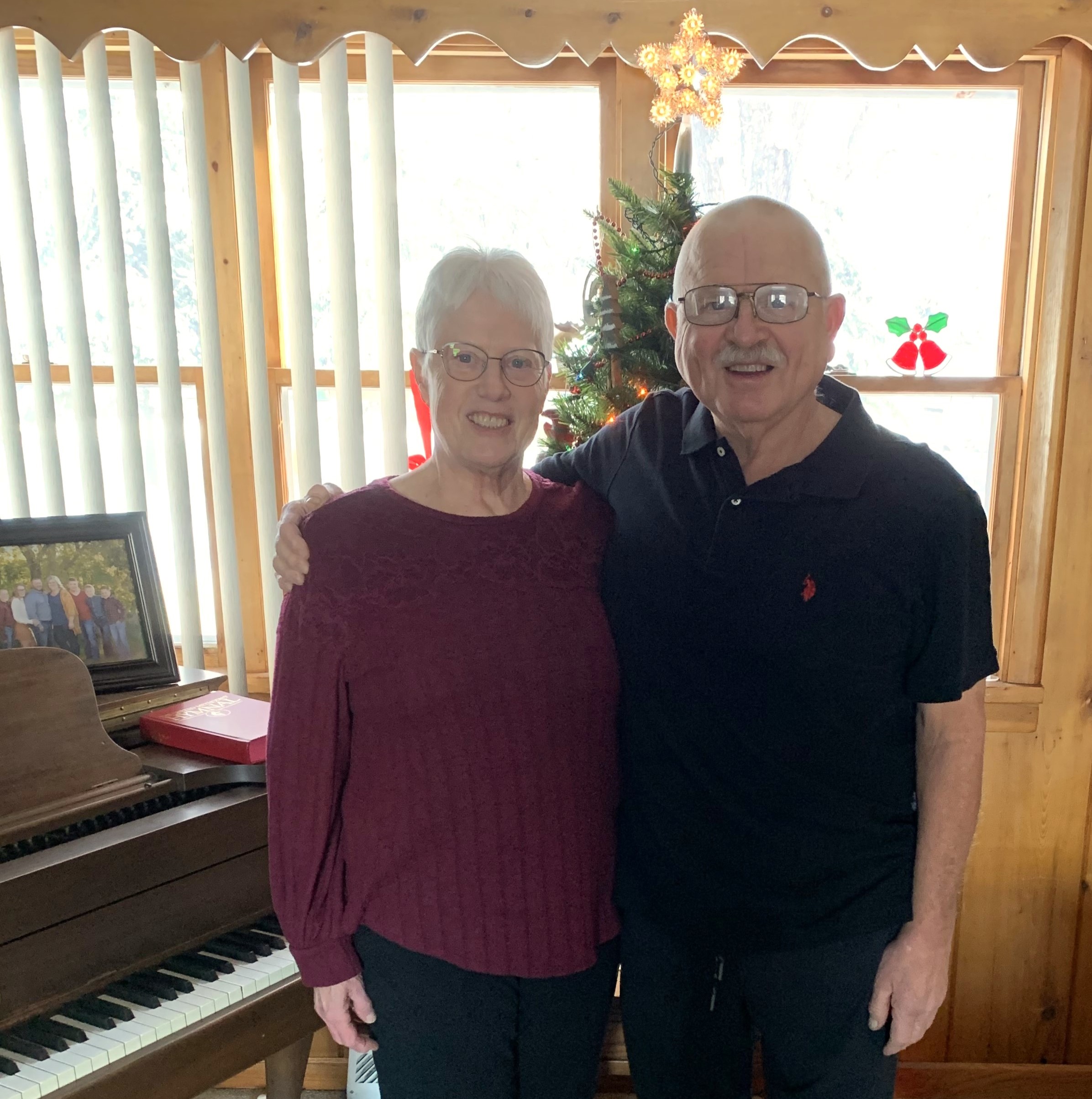 Jane and Gene standing in front of a Christmas tree and piano