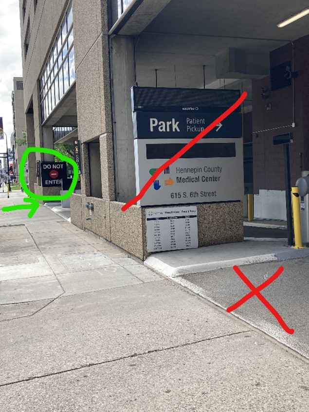 image of the parking ramp at 615 S 6th St. The entrance to the parking ramp has been crossed out with a red line. In the background of the image is a 'Do Not Enter' sign that is circled and marked with a green arrow