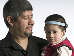 Man holding a child with a band around it's head holding a bone conduction device