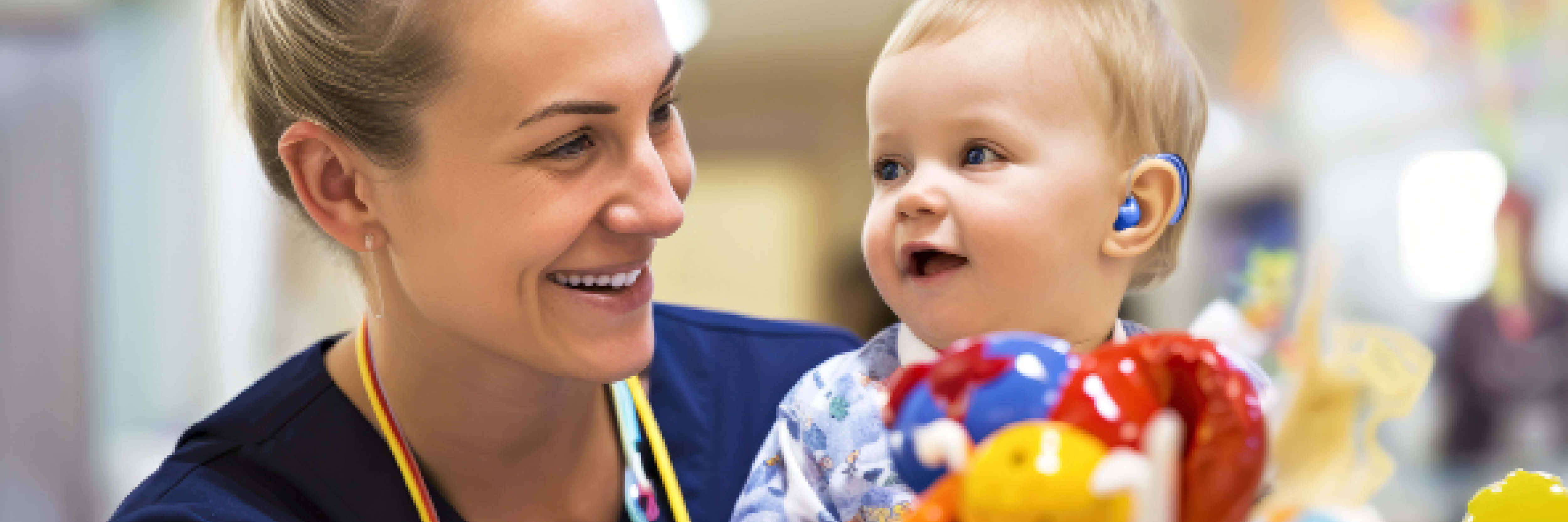 Photo of healthcare worker smiling at an infant wearing a hearing aid