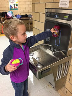 A young girl fills a water bottle at a drinking fountain water bottle filling station.