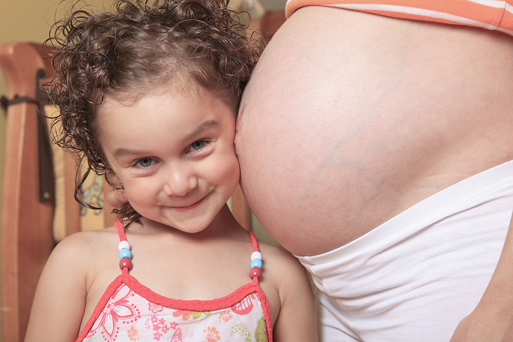 Young girl hugging pregnant mom's belly.